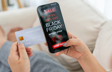 Person using app shop online holding smartphone with Black Friday sale ad and credit card ready for online payment, e-commerce promotions, digital marketing, online shopping and mobile transactions