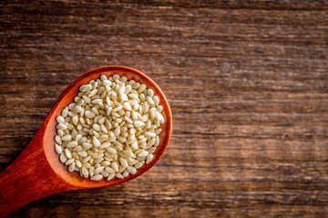 Roasted sesame seeds on spoon on wooden table. Top view.