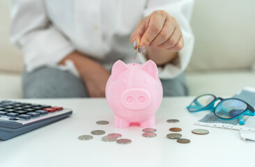 Person saving money inserting coin into pink piggy bank while calculating budget, personal finance, budgeting and financial planning at home with calculator, financial goal management, cost control