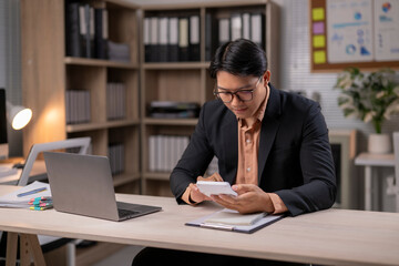 Fototapeta premium A man in a suit is sitting at a desk with a laptop and a calculator