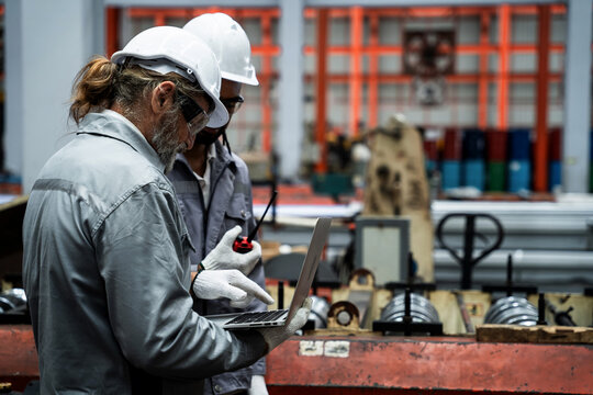 Two men in safety gear are looking at a laptop computer