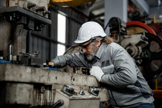 A man in a white hat and safety glasses is working on a machine - Powered by Adobe