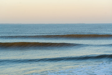 Tranquil ocean scene featuring evenly breaking waves under the gentle glow of early morning light. 