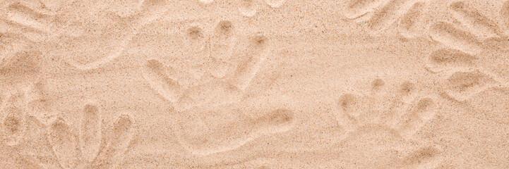 Background of people hand prints on dry light brown sea sand. Wide banner. Closeup. Top down view.