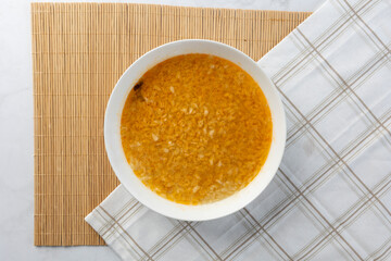 White bowl of yellow soup on bamboo mat