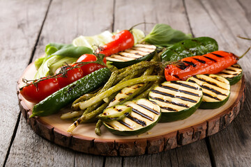 Grilled vegetables, including zucchini, peppers, and green beans, presented on a wooden board.