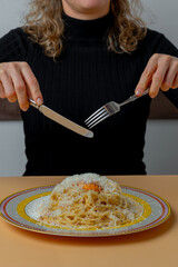 Girl with knife and fork eating carbonara pasta with egg yolk