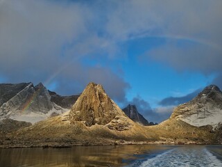 Beautiful snowy mountains over fishing village Reine in Lofoten islands, Norway, with partially frozen fjord and rainbow in winter at sunrise. Dramatic sky over snowy rocks and sea at dawn