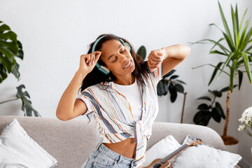 Cheerful, smiling authentic woman listening music in earphones enjoying in living room at home