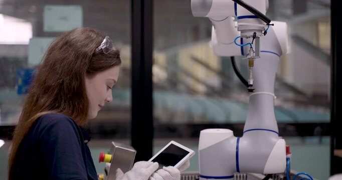 Student with long hair adjusts robot suction gripper using gloved hand during collaborative robot training inside smart factory simulation setup for automation movement handling education