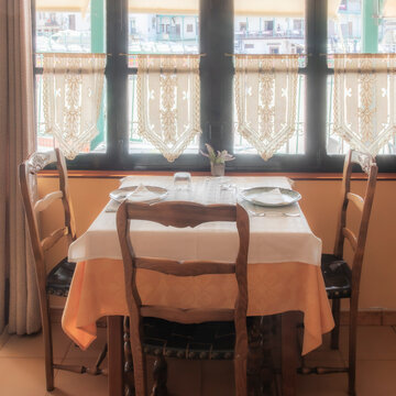 mesa preparada para dos comensales con un gran ventanal y finos visillos que da a la plaza mayor de Chinch&oacute;n, Madrid