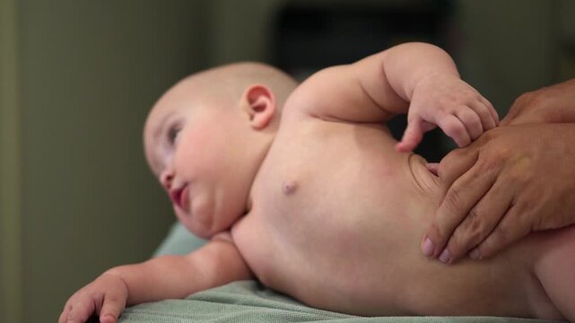 A baby is being massaged by a person. The baby is lying on a bed and the person is holding the baby's arm