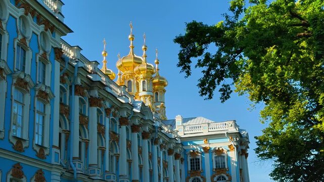 A low-angle horizontal shot of the richly decorated Catherine Palace in Tsarskoye Selo, highlighting its iconic azure blue and white facade, white columns, gilded ornaments, and the cluster of