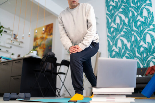 Crop anonymous male in sportswear doing lunges exercise while watching online tutorial on laptop during fitness training at modern home