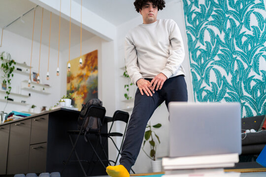 Crop anonymous male in sportswear doing lunges exercise while watching online tutorial on laptop during fitness training at modern home