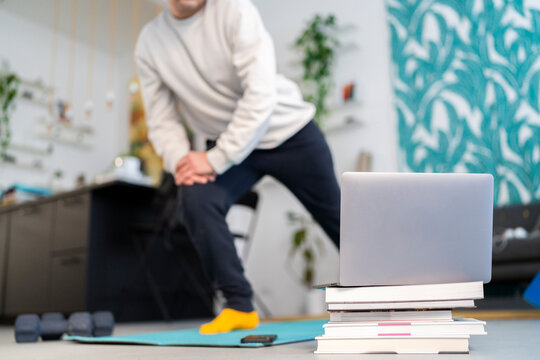 Crop anonymous male in sportswear doing lunges exercise while watching online tutorial on laptop during fitness training at modern home