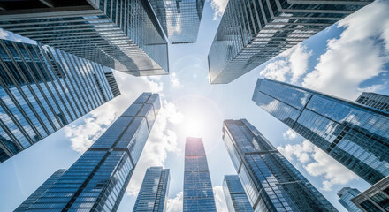 Modern skyscrapers in financial district, low angle view of glass office buildings against blue sky with sun flare, business success concept