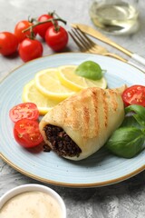 Piece of tasty grilled squid stuffed with mushrooms, basil, tomatoes, lemon and sauce on grey textured table, closeup