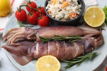 Raw squids, stuffing, rosemary, lemon and tomatoes on white tiled table, closeup