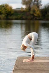 An adult woman practices yoga in nature near the water