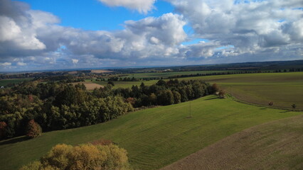 Obraz premium Beautiful sunny day with green fields and colorful trees on the horizon of the Czech countryside. Aerial drone view capturing the vibrant autumn landscape 