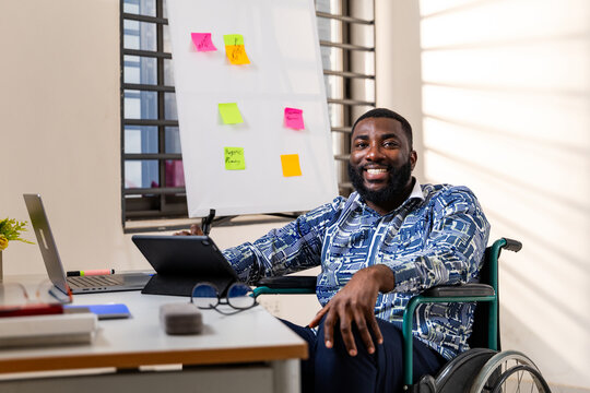 Happy African man in a wheelchair working productively in modern office, inclusion and accessibility