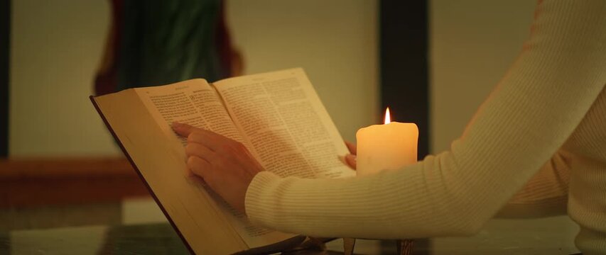 Person reading an open Bible by candlelight inside a catholic church close-up