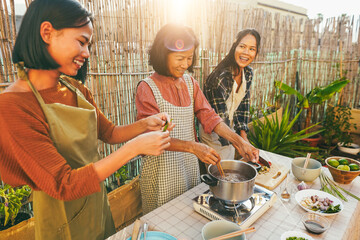 Asian family cooking thai food together at home patio outdoor - Mother and two daughters having fun preparing papaya salad for dinner at house backyard - Main focus on mum face