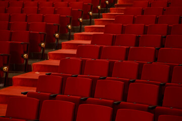 Fototapeta premium Close up view of red theater seats and illuminated aisle inside an empty auditorium