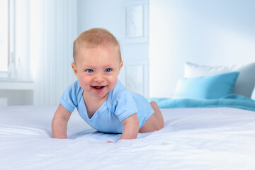 Portrait of a blonde, happy baby boy with blue eyes crawling on the bed