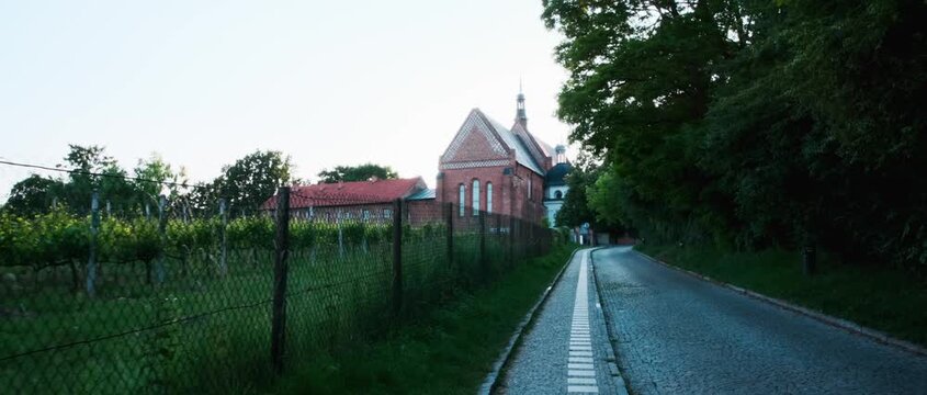 Sandomierz, Poland &mdash; Establishing shot of brick church by a vineyard and cobblestone lane, red-tiled roofs, dense trees, soft evening light, summer, cinematic travel footage, historical cityscape 4KHD