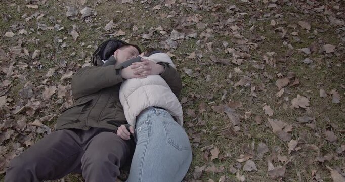 A loving couple enjoys a tender moment, embracing and kissing while lying on the ground amidst autumn leaves in a beautiful park.