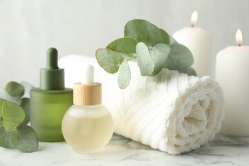 Beautiful spa composition with essential oils and burning candles on white marble table, closeup