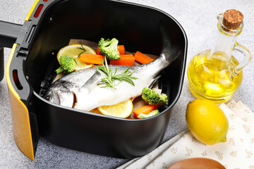 Raw fish, lemon and vegetables in air fryer on light grey table, closeup