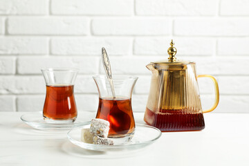 Tasty Turkish tea in glass cups, teapot and sweets on white marble table against brick wall