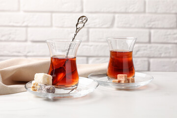 Tasty Turkish tea in glass cups, brown sugar and sweets on white marble table against brick wall