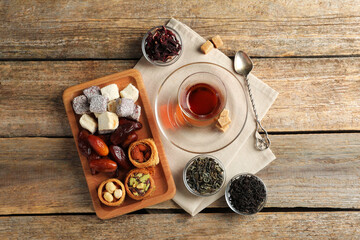 Traditional Turkish tea in glass, dry leaves and sweets on wooden table, flat lay
