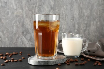 Tasty iced coffee, milk and beans on black wooden table