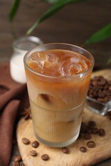 Tasty iced coffee in glass, milk and beans on wooden table, closeup