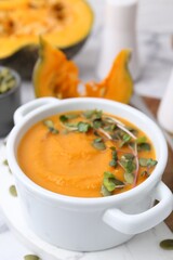 Delicious pumpkin soup with seeds and microgreens in bowl on table, closeup