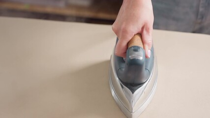 Hand view of hand holding pressing iron moving round cloth spread on ironing table as steam comes out, focusing on skillful technique, delivering neat finishing, refining garment details