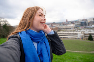 Young woman in blue scarf enjoys a scenic view of the city from a hilltop on a cloudy day