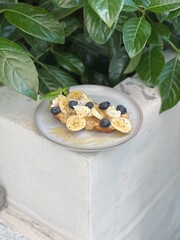 Peanut butter banana toast with blueberries, chia and honey on ceramic plate, outdoor