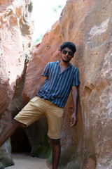 A man in a striped shirt and khaki shorts stands in a cave
