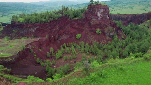 Racos volcano in Brasov, Romania: Unique volcanic crater landscape with red earth, lush green trees and surrounding hills