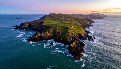 Aerial vista of a hilly island with verdant fields and scattered structures, meeting rocky coastline and an expansive ocean. The sunset casts a warm glow