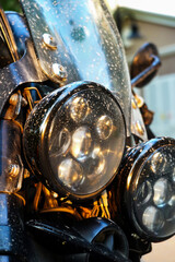 Rain-spotted headlamp of a vintage motorcycle glows under golden hour light-raw, rugged and real,...