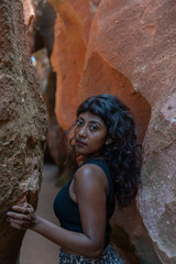 A woman with long hair stands in front of a large rock