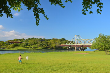Person holding white net on green lawn overlooking Dongshan River with red-decked white truss...