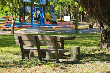 Wooden bench on grass lawn facing vibrant playground with slides and climbing structures in...